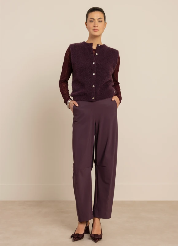 Vrouw draagt een bruin geruit gilet met bijpassende wijde pantalon en een witte blouse, handen in de zakken. De set laat zien hoe tailoring met print zorgt voor een stijlvolle en moderne look.