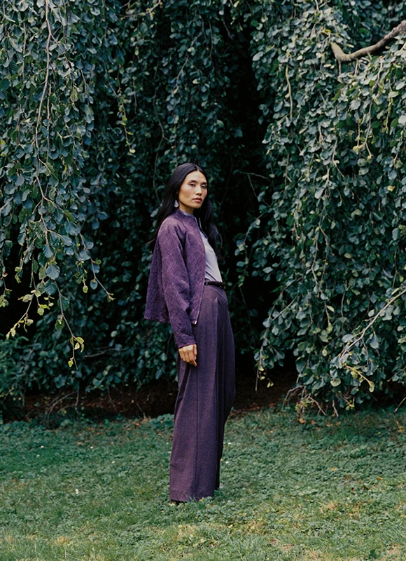 Drie vrouwen staan dicht bij elkaar en dragen outfits in diepe tinten zoals bordeaux, paars en roze. De combinatie van verschillende stoffen en silhouetten geeft de look een krachtige en modieuze uitstraling.