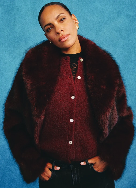 Vrouw draagt een felrode top met textuur en een bijpassende broek en kijkt opzij tegen een neutrale achtergrond. De ton-sur-ton styling benadrukt de kracht en energie van de kleur rood in de outfit.