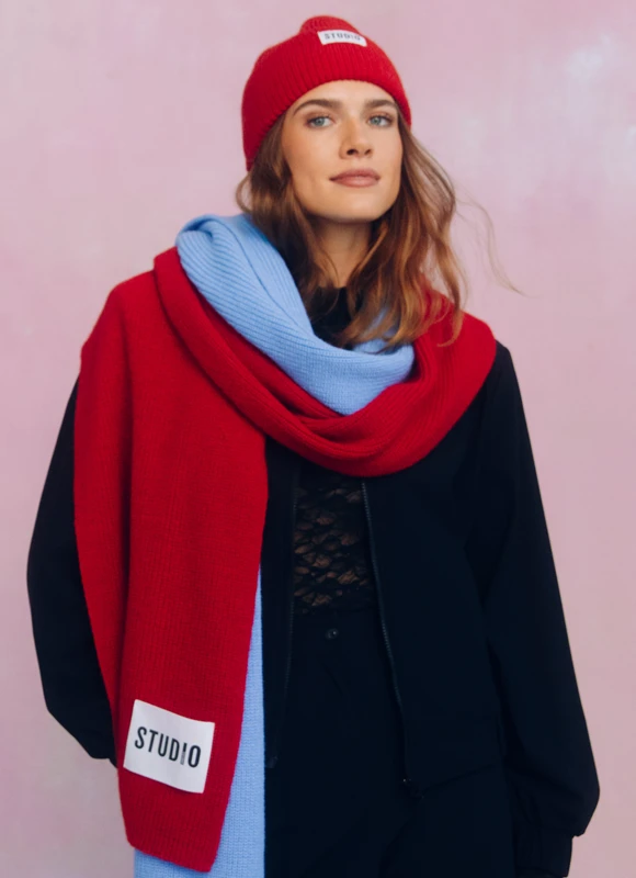 Vrouw draagt een rood gestreepte blouse met wijde denim jeans en staat ontspannen met haar handen in haar zij tegen een neutrale achtergrond. De combinatie van rood en denim geeft de look een casual en tijdloze uitstraling.