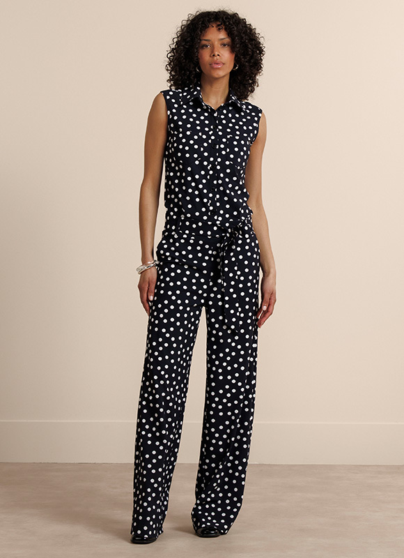 Vrouw staat ontspannen en draagt een donkerbruine outfit met een losvallende top en wijde pantalon. De ton-sur-ton look geeft een elegante en moderne uitstraling.