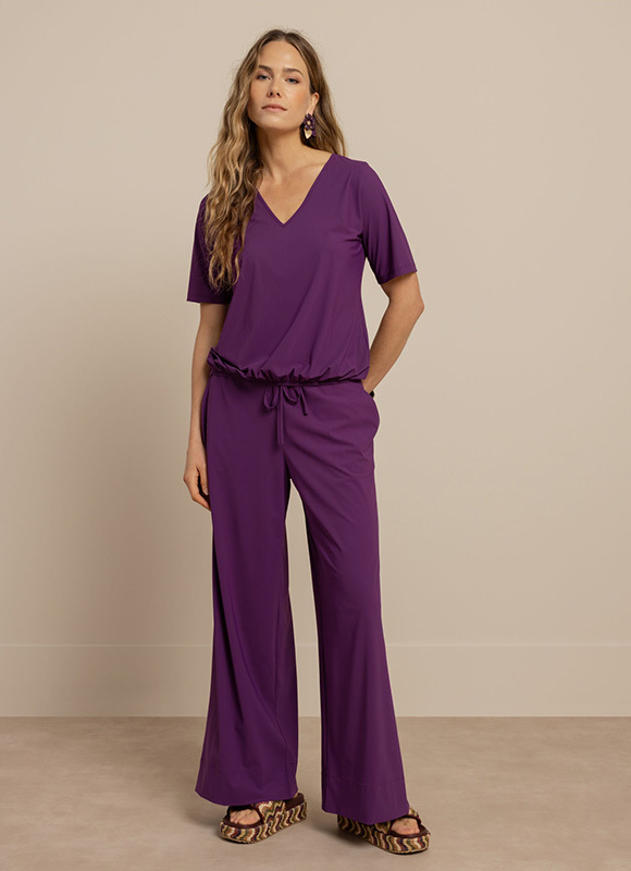 Vrouw staat rechtop en draagt een donkerblauwe top met schouderdetails gecombineerd met een bijpassende korte broek en sneakers. De outfit heeft een sportieve en eigentijdse uitstraling.