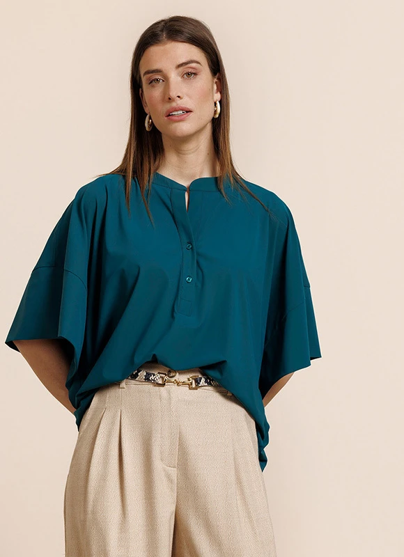 Vrouw draagt een donker blazer met een subtiele ruit en een paarse top en houdt de revers vast terwijl ze rechtop staat. De combinatie van lagen en diepe kleuren geeft de outfit een elegante en krachtige uitstraling.