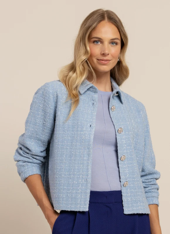 Close-up van een beige jasje met rijke textuur en knopen, gecombineerd met een paarse broek. De stofstructuur en details geven de outfit een luxe en verfijnde uitstraling.
