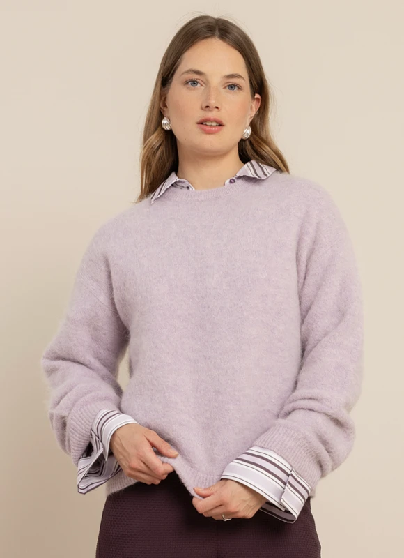 Vrouw draagt een donker blazer met een subtiele ruit en een paarse top en houdt de revers vast terwijl ze rechtop staat. De combinatie van lagen en diepe kleuren geeft de outfit een elegante en krachtige uitstraling.