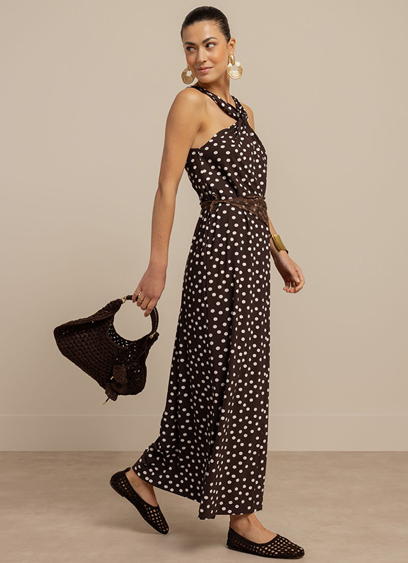 Vrouw draagt een blouse met print en een donkere broek en staat zelfverzekerd in een klassieke interieursetting. De combinatie van het patroon en de elegante houding geeft de outfit een krachtige en modieuze uitstraling.