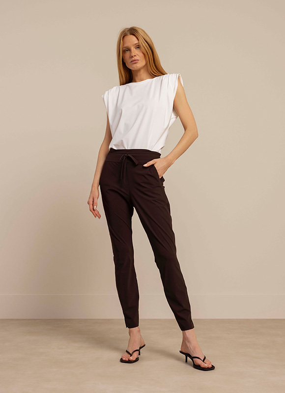 Vrouw draagt een groene top met korte mouwen gecombineerd met een zwarte broek en hakken, staand in een neutrale studio setting. De outfit laat een frisse en zakelijke look zien met een subtiele print.