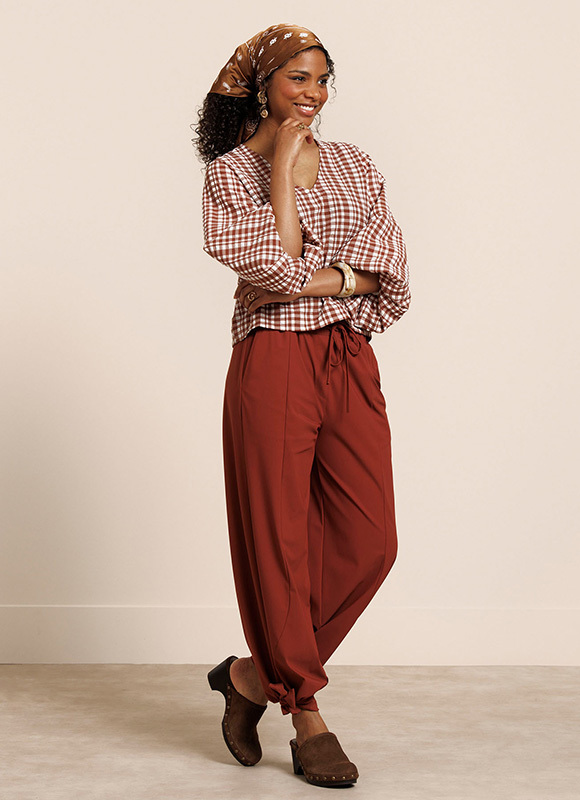 Vrouw staat leunend tegen een klassieke zuil en draagt een beige top over een wit overhemd met een bijpassende broek. De gelaagde outfit laat zien hoe neutrale tinten zorgen voor een rustige en stijlvolle look.