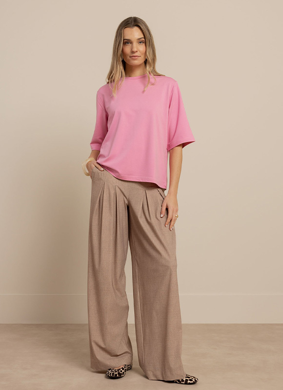Vrouw draagt een felroze top met driekwart mouwen gecombineerd met een beige flowy pantalon met wijde pijpen. De comfortabele broek zorgt voor een elegante en luchtige zomerse look.