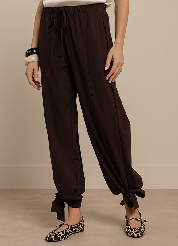 Donkerbruine ballonbroek met losse pasvorm en strikdetails bij de enkels. De luchtige broek wordt gecombineerd met ballerina’s met dierenprint voor een comfortabele en trendy look.
