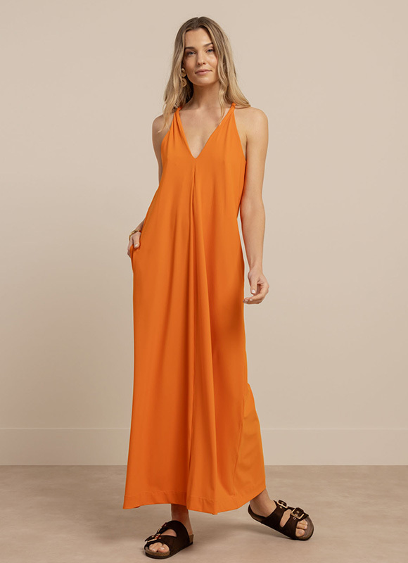 Vrouw draagt een lange oranje zomerjurk met diepe V-hals en luchtige pasvorm. De maxi jurk is gecombineerd met zwarte sandalen voor een effortless zomerse look.