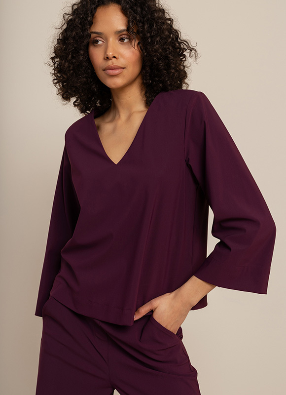 Vrouw zit op een bank en draagt een taupekleurig pak met een blouse en hakken, gecombineerd met een mouwloos vest. De outfit laat zien hoe nieuwe kleurcombinaties zorgen voor een rustige en stijlvolle uitstraling.