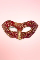 Handmade Venetian masquerade mask flat lay against a light pink background.