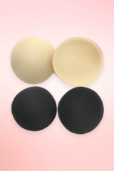 Round foam bra pad inserts in beige and black, two pairs shown flat on a pink background.