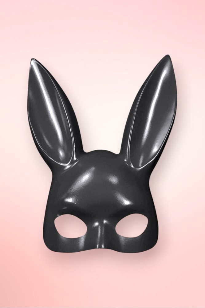 Isolated front view of a glossy black bunny masquerade mask on a pink background.