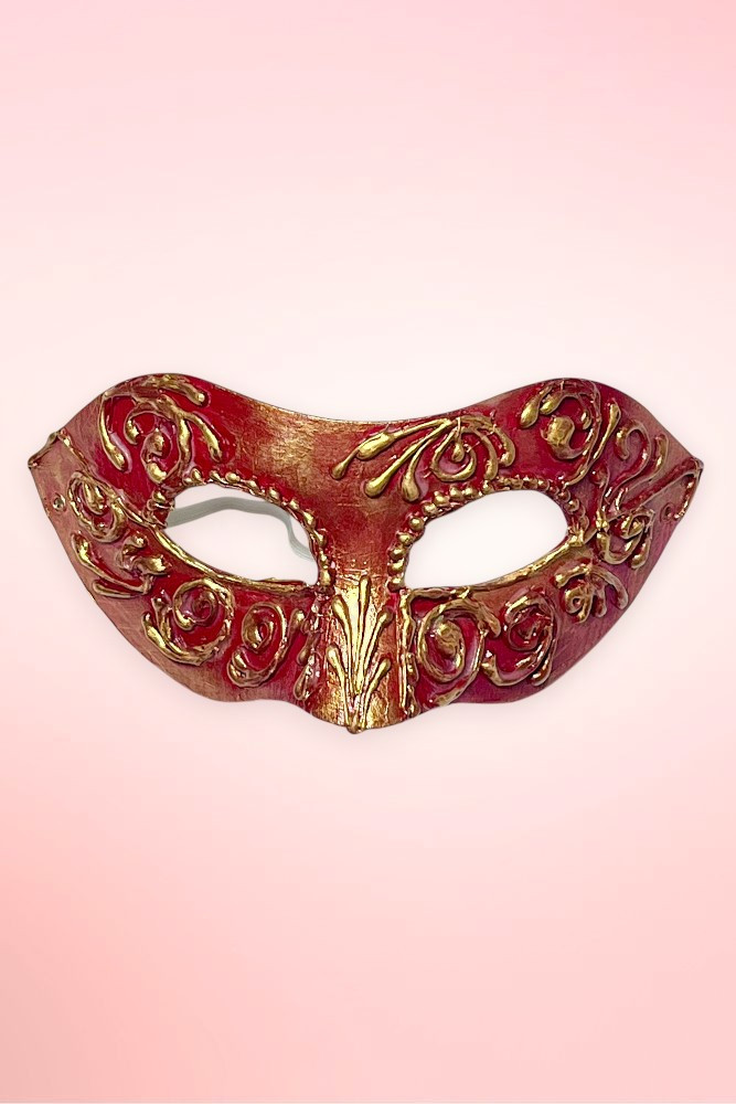 Handmade Venetian masquerade mask flat lay against a light pink background.