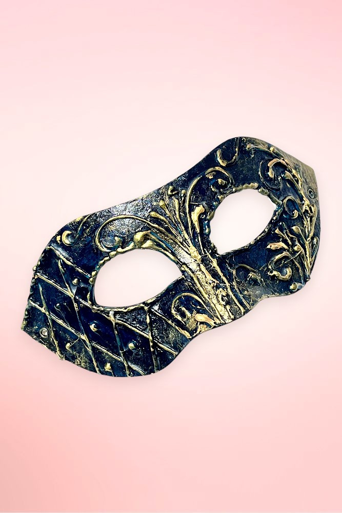 Handmade navy and gold Venetian masquerade mask angled right on pink background.
