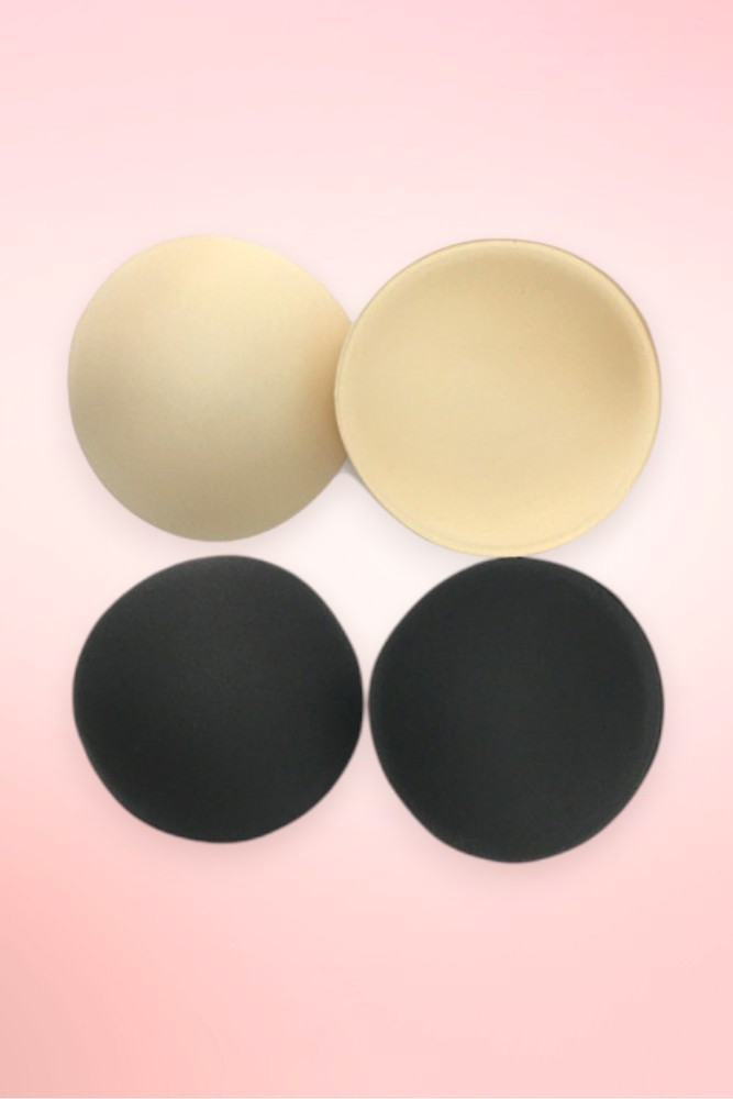 Round foam bra pad inserts in beige and black, two pairs shown flat on a pink background.