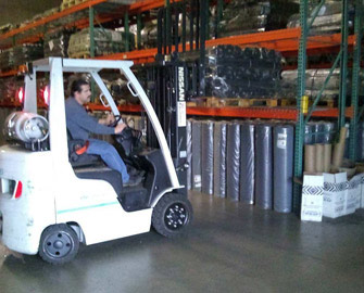 Man driving a white forklift in a Rubber-Cal Warehouse