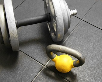 A dumbbell and kettlebell resting on Interlocked rubber tiles