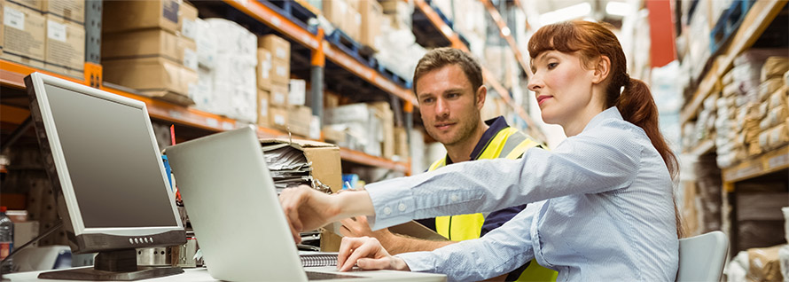 A full warehouse with a single employee, working from his laptop atop a stack of boxes.