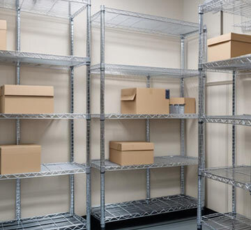 Freestanding chrome wire shelving with white and black boxes inside of it.