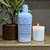 a 4oz white bottle of lotion from moccasin bend soap company in the scent Love Potion next to a lit candle and potted plant
