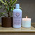 a 4oz white bottle of lotion from moccasin bend soap company in the scent Amber Oasis next to a lit candle and potted plant