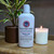 a 4oz white bottle of lotion from moccasin bend soap company in the scent Plain Ole next to a lit candle and potted plant