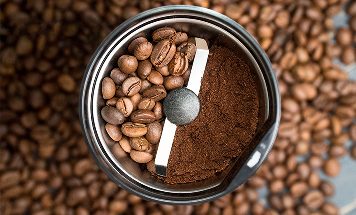 a coffee grinder holding ground and unground coffee on either side of the blade
