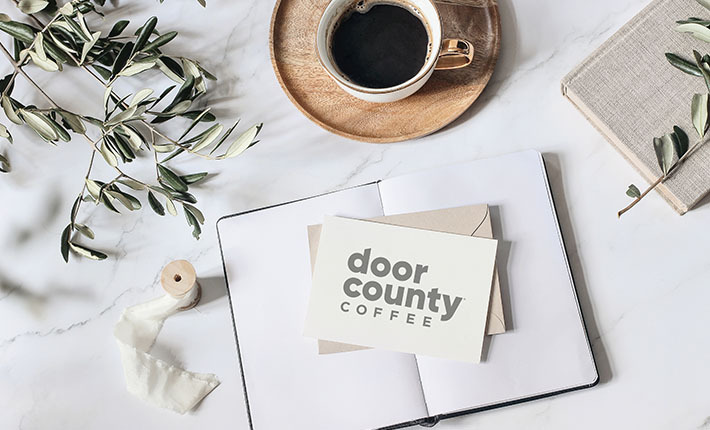 elegant writing scene with cappuccino on wood coaster, olive branch, notebooks and stationary