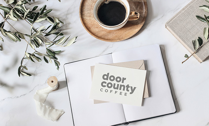 elegant writing scene with cappuccino on wood coaster, olive branch, notebooks and stationary