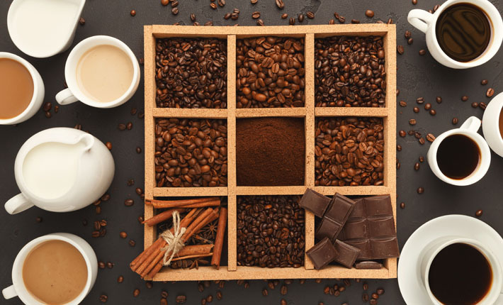 a bento box holding coffee beans, cinnamon, and chocolate between an assortment of coffee mugs and other vessels