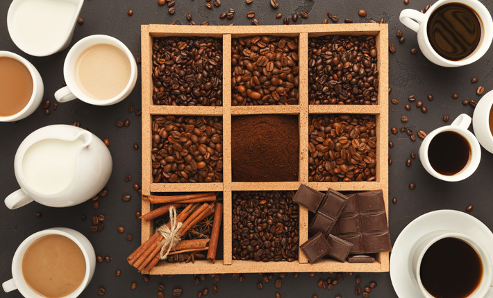 a bento box holding coffee beans, cinnamon, and chocolate between an assortment of coffee mugs and other vessels