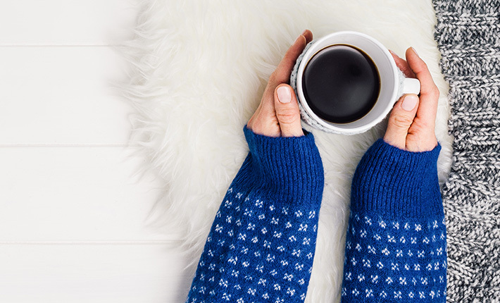 a pair of hands cradling a mug of coffee on a furry blanket