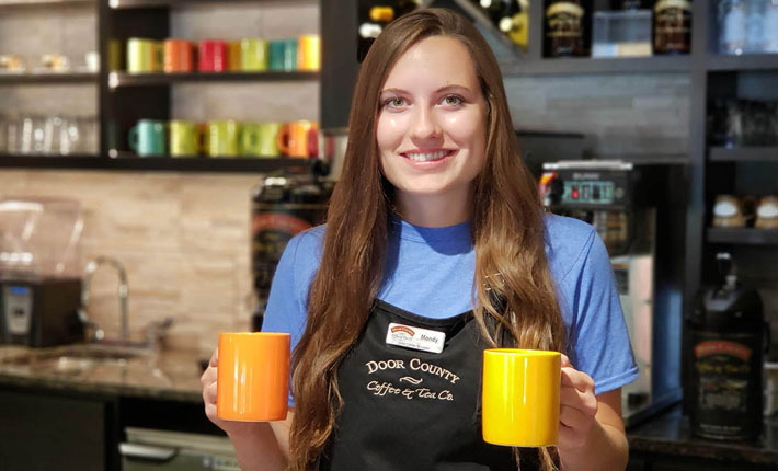 female barista holding two colorful mugs in cafe