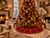 Luxury 84-inch red velvet Christmas tree skirt by SADE New York, featuring embroidered gold Christmas bells, sparkling rhinestone trim and elegant detailing beneath a grand Christmas tree in a luxurious living room.