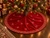 Luxury red velvet Christmas tree skirt by SADE New York, featuring a sparkling geometric rhinestone border and delicate crystal motifs, displayed beneath an elegant Christmas tree with red and gold ornaments, warm lights, and holiday gifts.