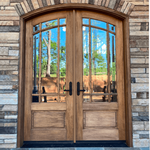 Mahogany 9 Lite arch top double door with clear bevel glass shown with a stone surround on a covered porch for refined style and curb appeal. Available at GrandEntryDoors.com.