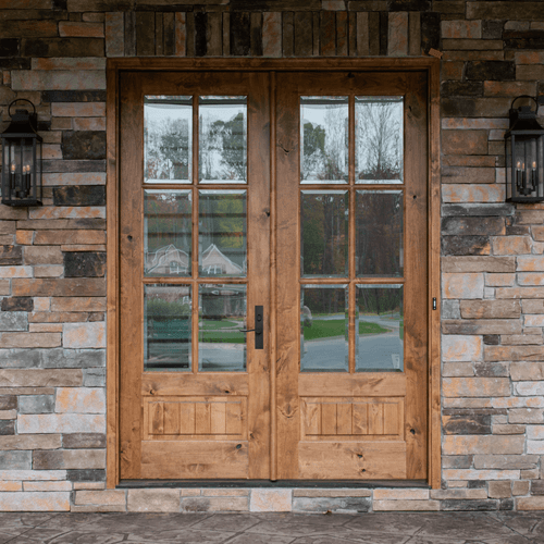 Knotty alder 6 Lite double front entry door featuring clear bevel glass and rich wood grain, shown on a stone exterior home for rustic elegance and timeless craftsmanship. Available at GrandEntryDoors.com.
