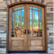 Mahogany 9 Lite arch top double door with clear bevel glass shown with a stone surround on a covered porch for refined style and curb appeal. Available at GrandEntryDoors.com.