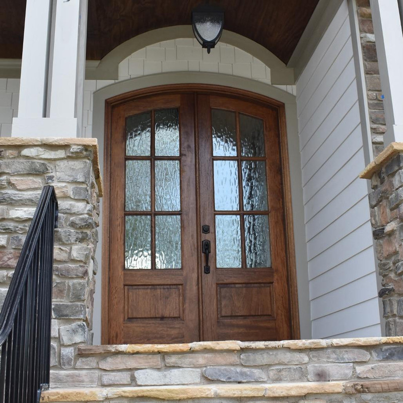 Beautiful flemish glass 6 lite arch top mahogany double door featured on a covered porch, perfect blend of style and protection. Available at Grandentrydoors.com.
