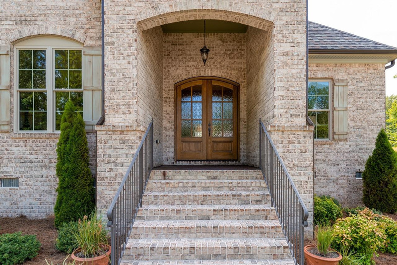 Light-finished flemish glass 6 lite arch top mahogany double door enhances a classic brick home with elegance and warmth. Available at Grandentrydoors.com.