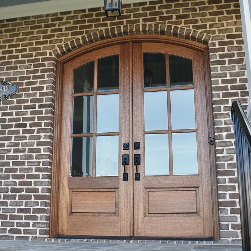 Clear bevel glass 6 lite arch top mahogany double door showcased on a traditional brick home for a timeless entrance. Available at Grandentrydoors.com.