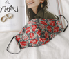 a silk lined red floral Sainted Sisters Mask posed with a fashion magazine