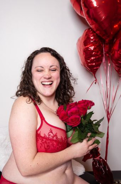 A woman wearing a luxury, high quality red French bra by Empreinte holds roses and laughs