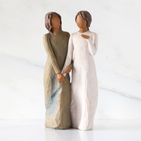 Front view: Figure of two women with darker skin tones in different colored dresses, standing arm in arm