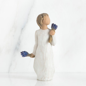 Small girl figurine wearing white dress holding two blue flower bouquets in each hand