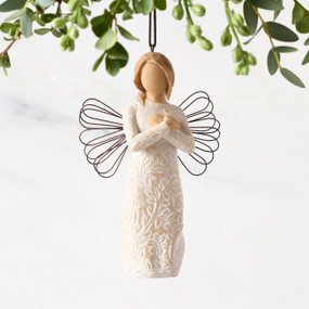 Front view of figure in cream dress carved with symbols of nature with wire wings, hands folded at chest around gold heart, ornament hook on head