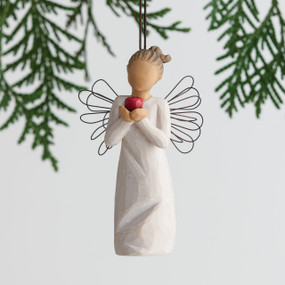 Front view of angel ornament with brown hair in high pony tail leaning forward and holding a red apple up to her face with both hands. Brown string attached to top of angel ornament